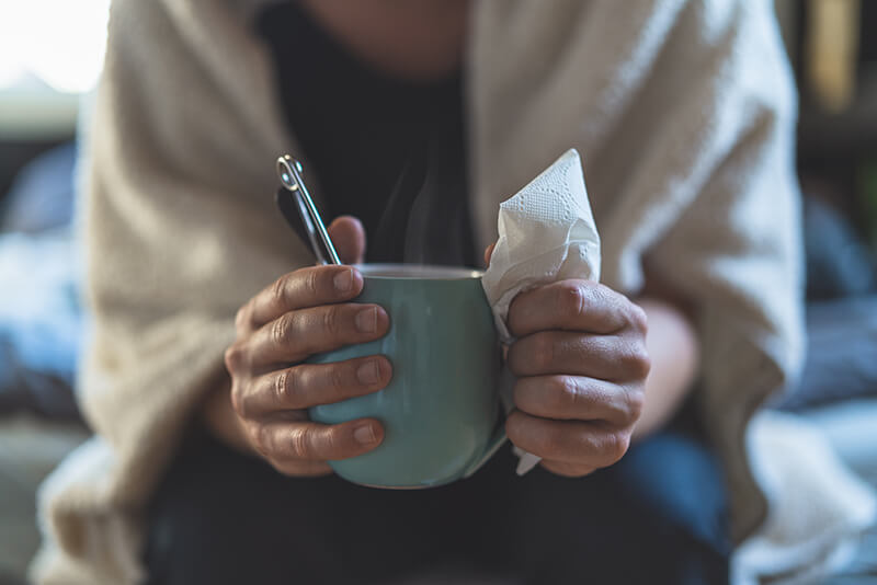 En förkyld person som håller en varm kopp te och papper